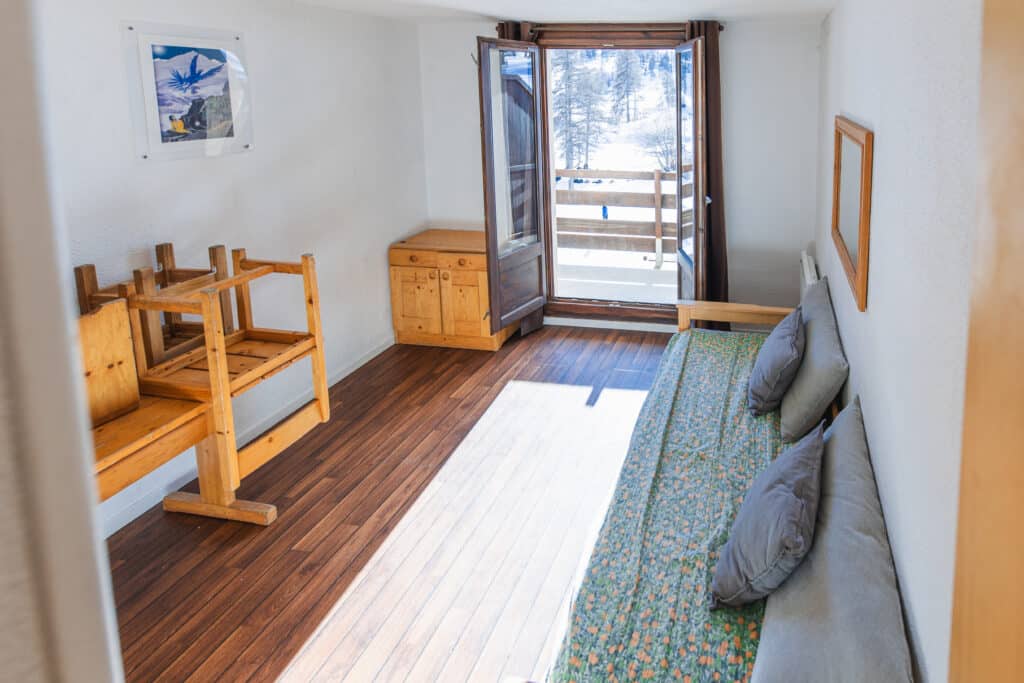 Séjour du studio 4 personnes avec banquette, table en bois et accès au balcon